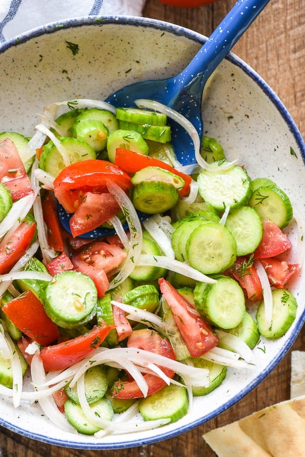 Easy Cucumber and Tomato Salad in a speckled white and blue bowl to pair with burgers and hot dogs.