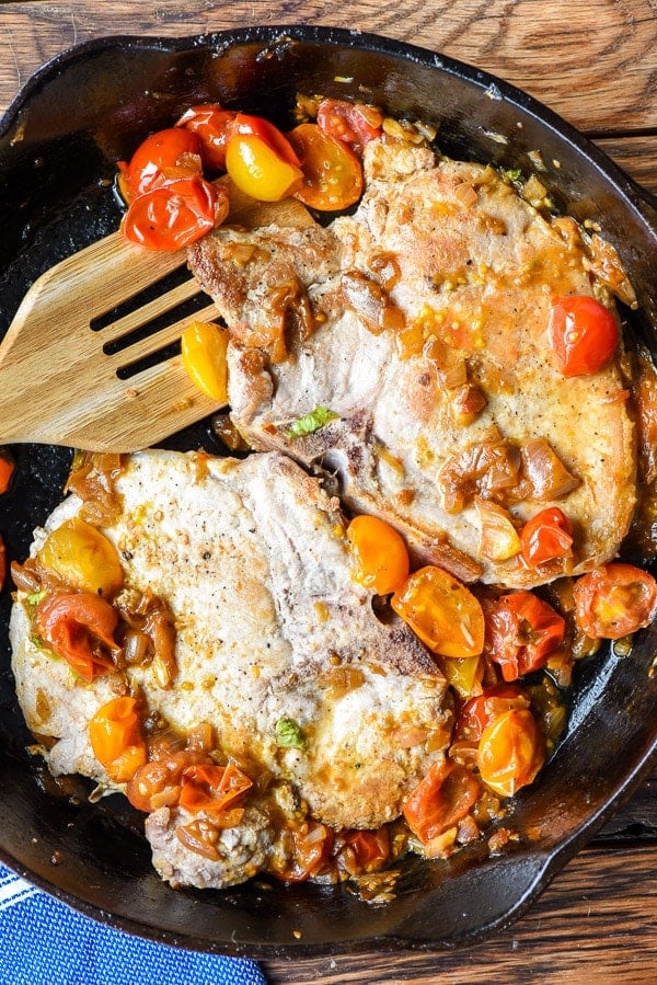 Two Pork Chops in a skillet with burst tomatoes