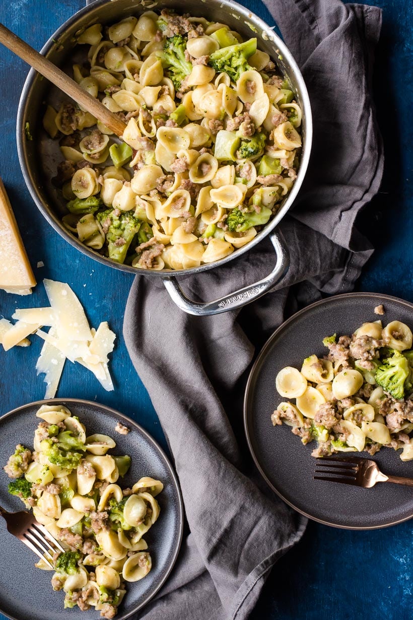 Orecchiette with Sausage and Broccoli in a skillet with two plates of pasta