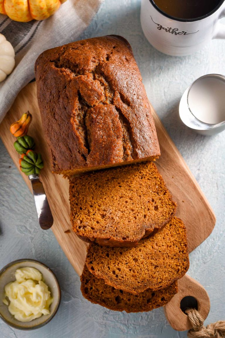 Loaf of pumpkin bread on a cutting board, surrounded by coffee mug and cream.