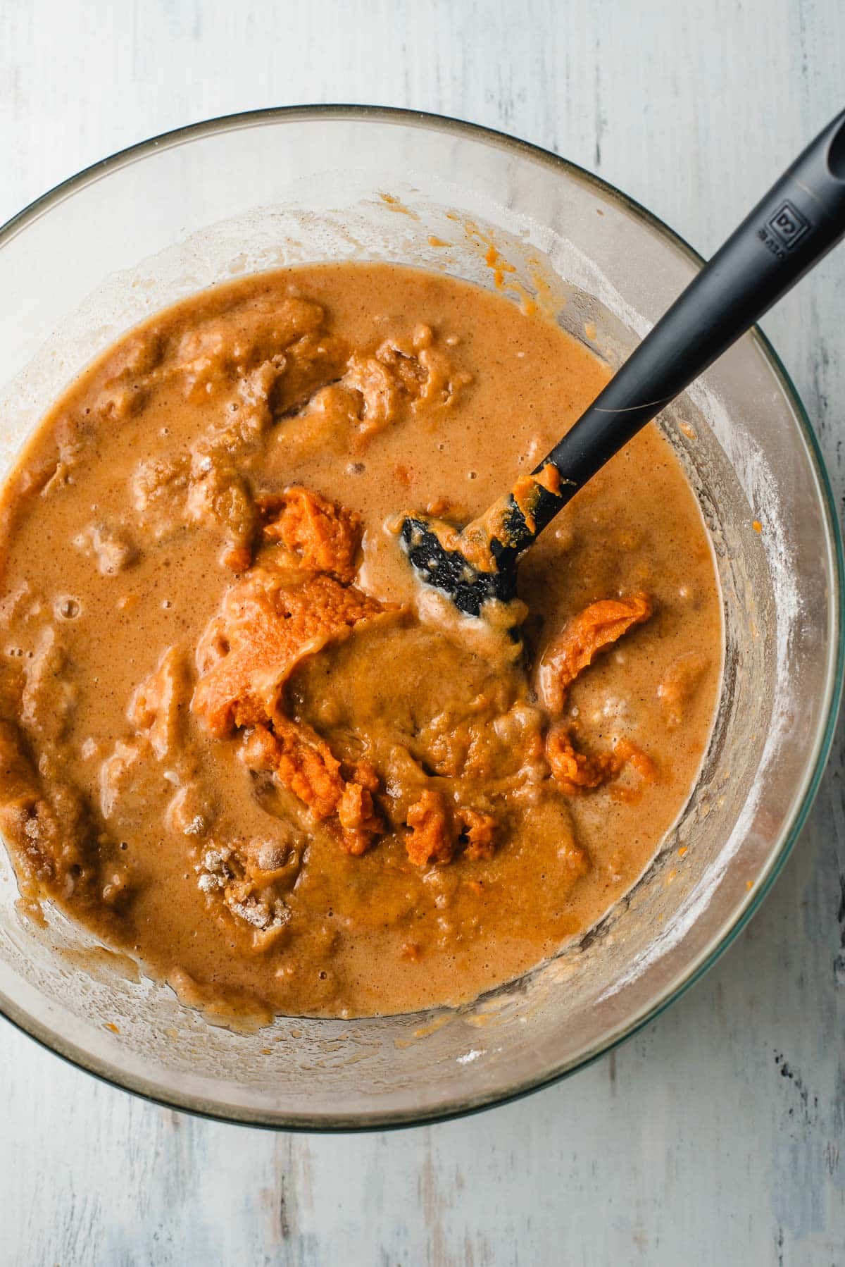 Pumpkin puree, vegetable oil, eggs, and water mixed with flour and spices in a glass bowl.