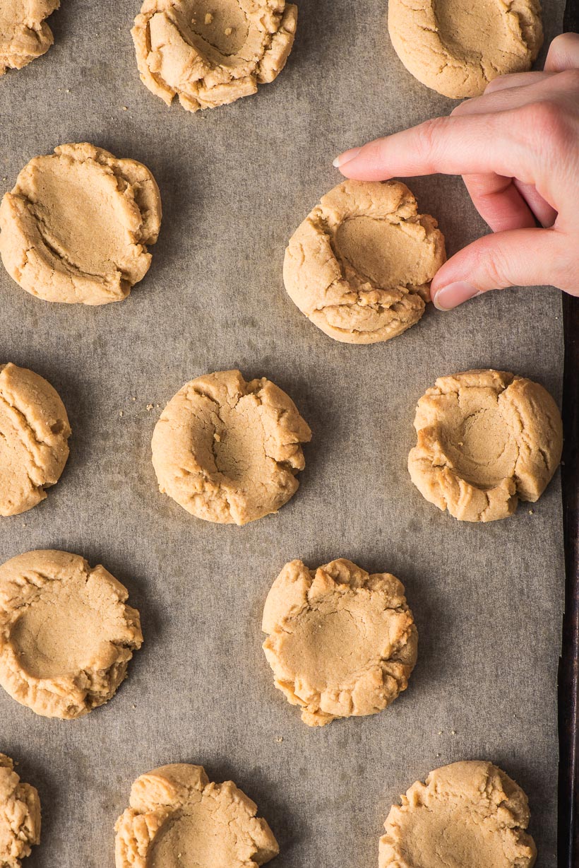 Peanut butter thumbprint cookies with a hand grabbing a cookie