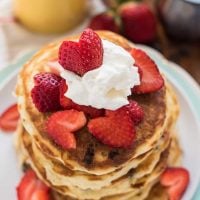 Stack of chocolate chip pancakes topped with strawberry hearts and whipped cream.