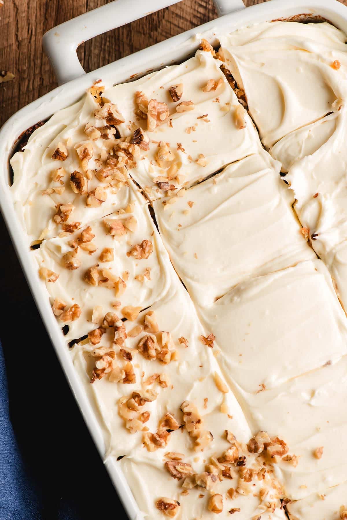 Carrot sheet cake with cream cheese frosting, sliced and partially sprinkled with pecans.