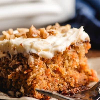 Slice of carrot sheet cake with cream cheese frosting, sprinkled with pecans.