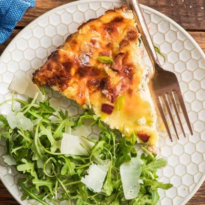 Slice of crustless quiche lorraine on a plate with an arugula salad.