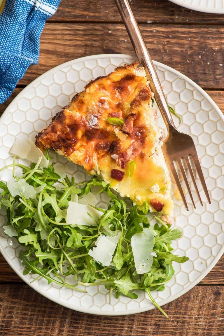 Slice of crustless quiche lorraine on a plate with an arugula salad.