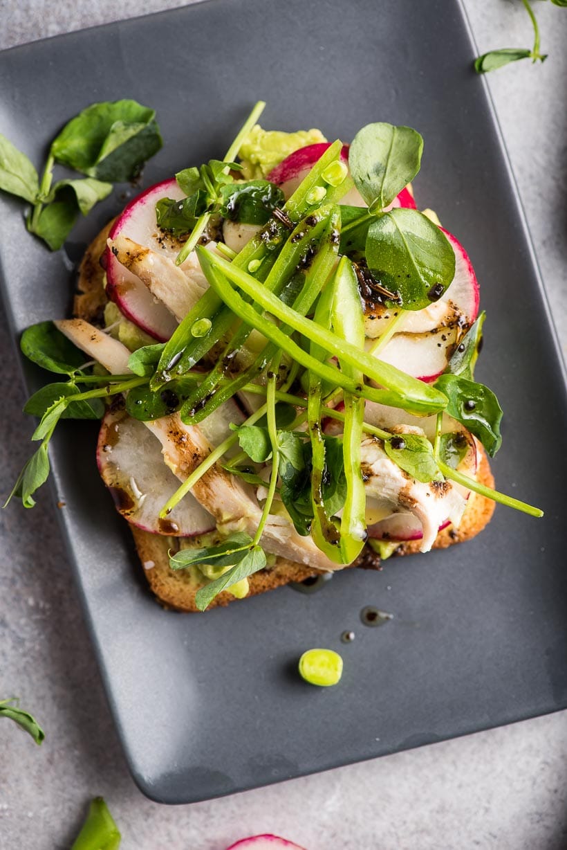 Avocado Toast with Radish, Chicken, and Peas on a black plate