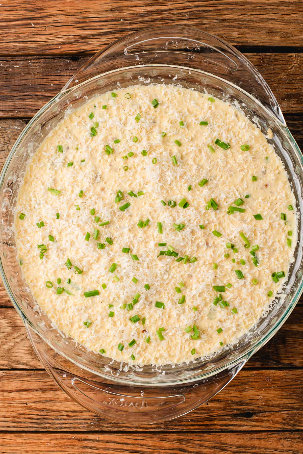 Unbaked egg custard in a glass pie dish topped with Parmesan and chives.