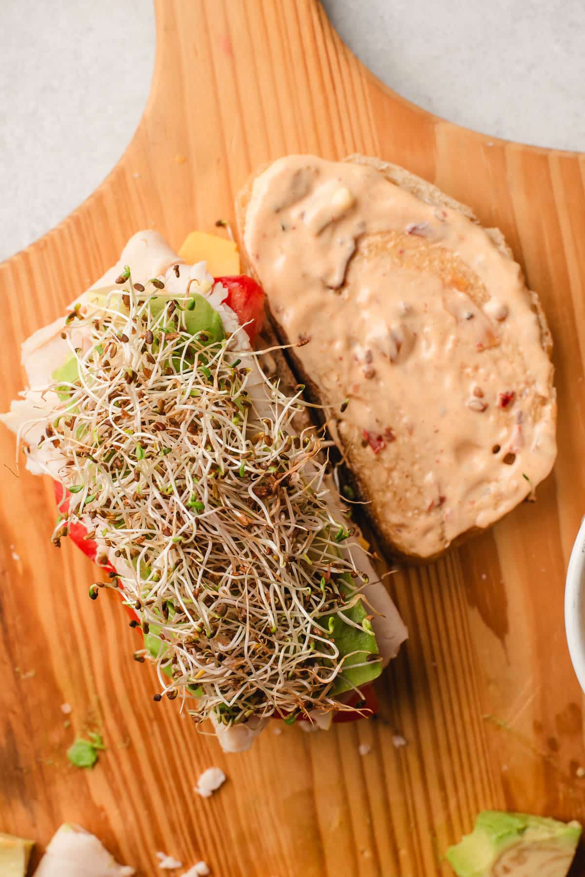 Two slices of bread stacked with turkey, cheese, avocado, tomato, sprouts, and chipotle mayo.