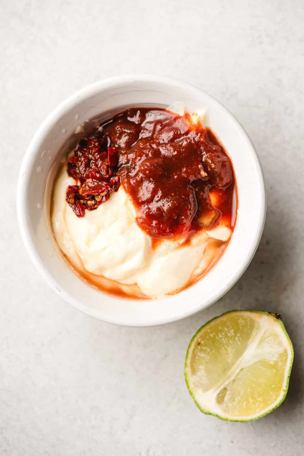 Mayonnaise and chipotle peppers in adobo in a bowl, with a halved lime beside it.