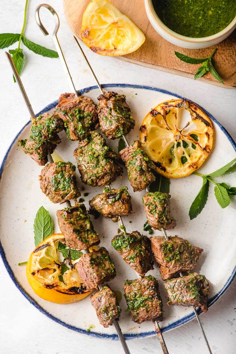 Steak Kabobs on a white and blue plate with grilled lemons