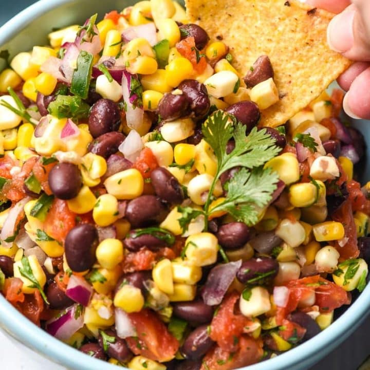 A tortilla chip scoops into a bowl of black bean and corn salsa.