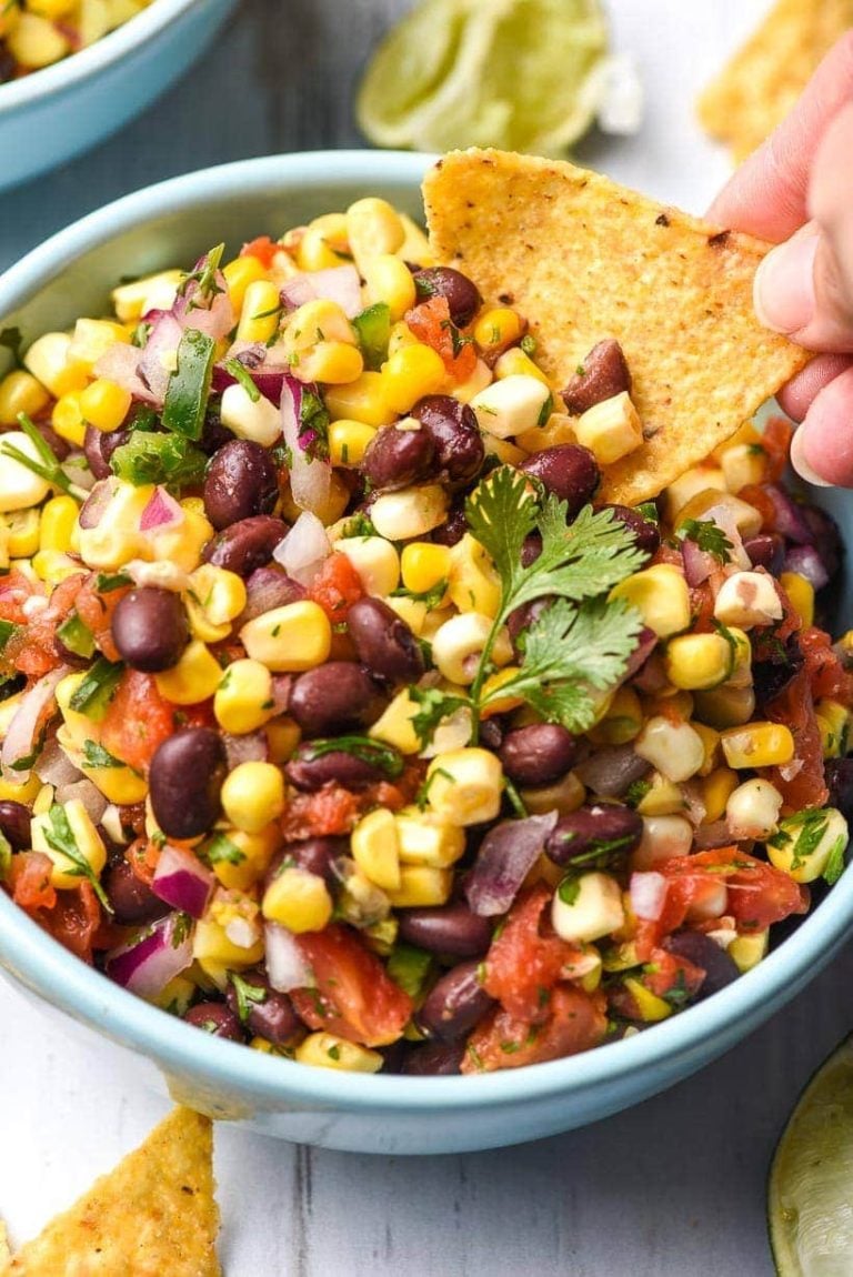 A tortilla chip scoops into a bowl of black bean and corn salsa.