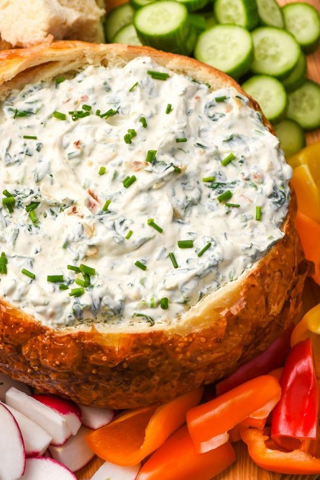 spinach dip in a sourdough bread bowl surrounded by fresh sliced vegetables