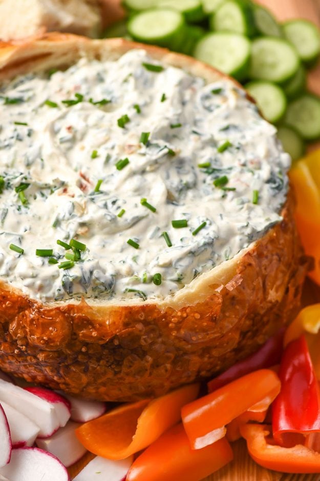 spinach dip in a bread bowl surrounded by fresh sliced vegetables