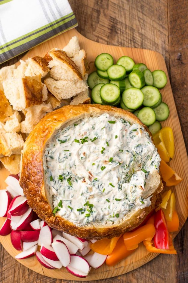 overhead of a spinach dip bread bowl on a wooden serving tray with fresh veggies