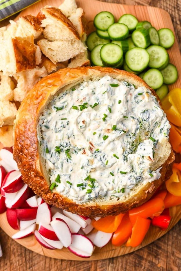 Overhead view of spinach dip in a bread bowl surrounded by fresh sliced vegetables