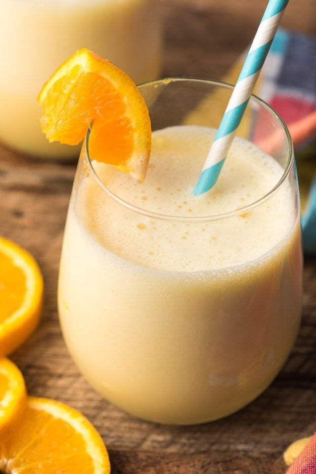 A glass of orange julius with a straw on a wooden table with orange slices
