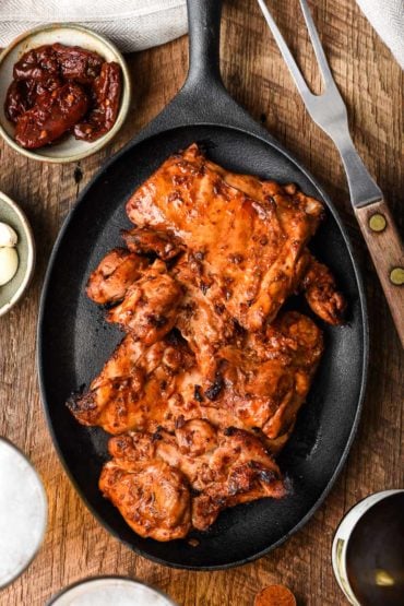 image of grilled spicy chicken thighs in a skillet, surrounded by chipotle pepeprs and spices