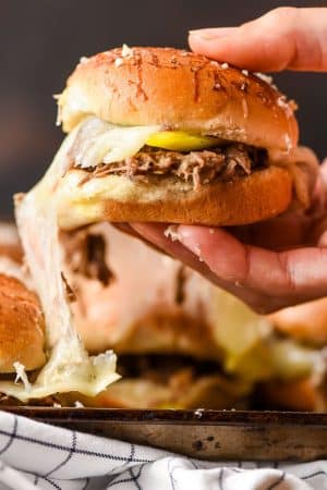 A hand grabs a pulled roast beef slider from a baking tray.