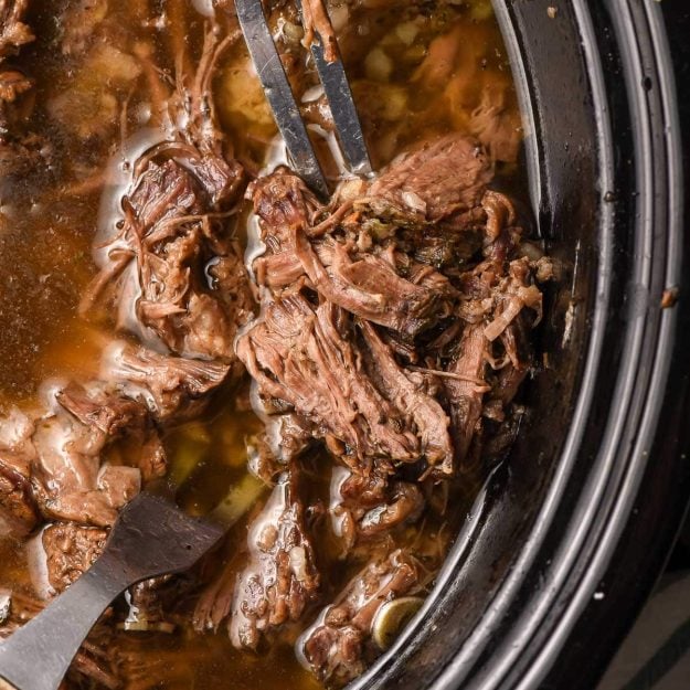 Meat fork stabbing into pulled beef in a crock pot