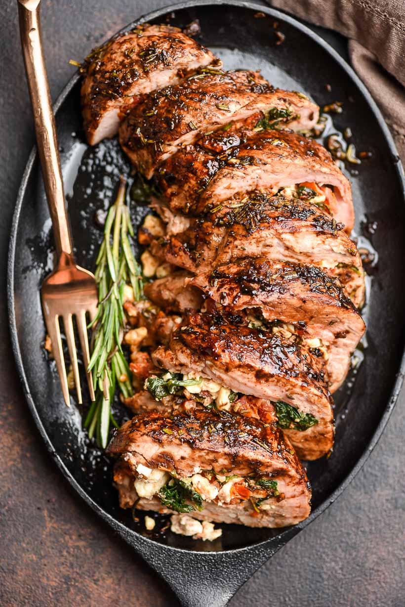 Stuffed Pork Tenderloin cuts on an iron skillet with herbs and a fork
