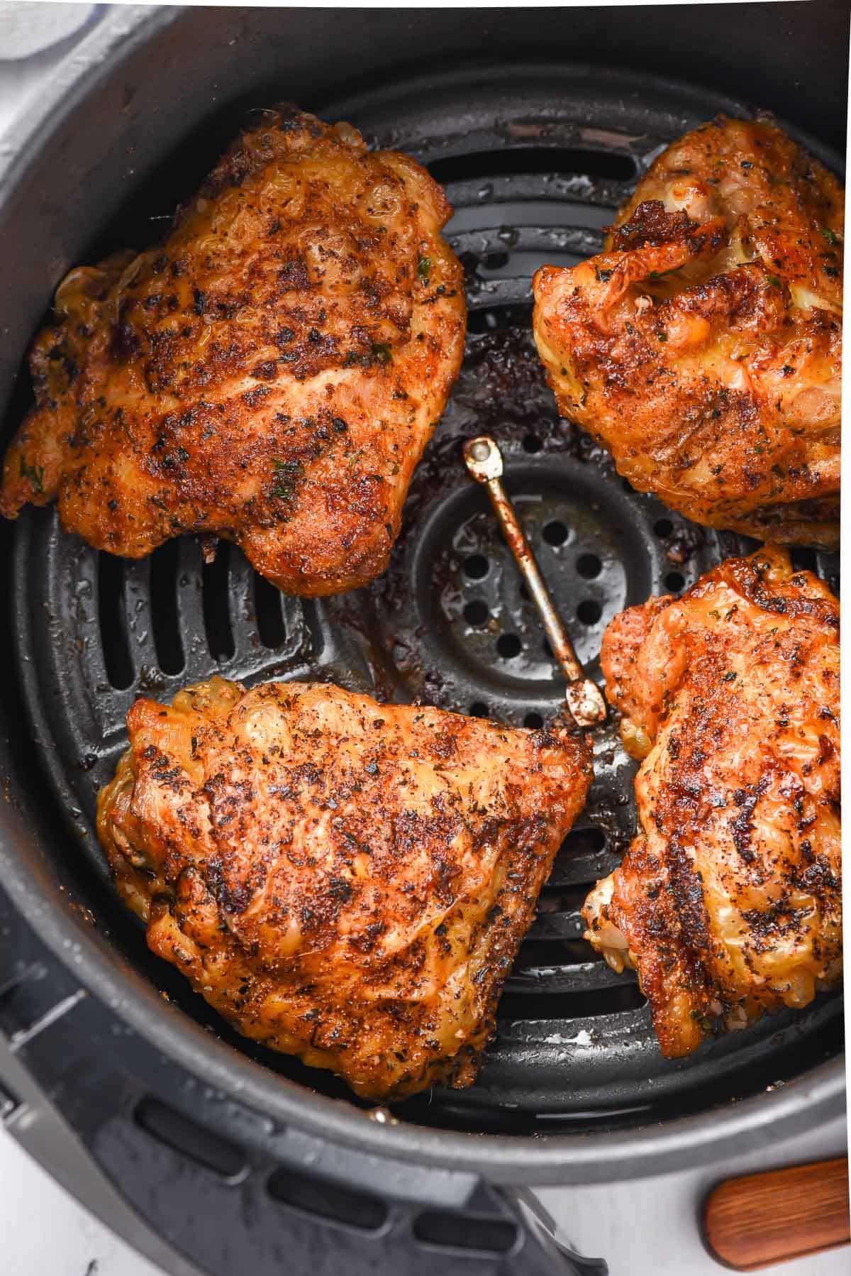 Four seasoned chicken thighs in an air fryer basket.