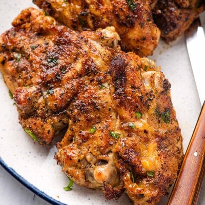Bone in chicken thigh seasoned and air fried, on a blue rimmed white plate.