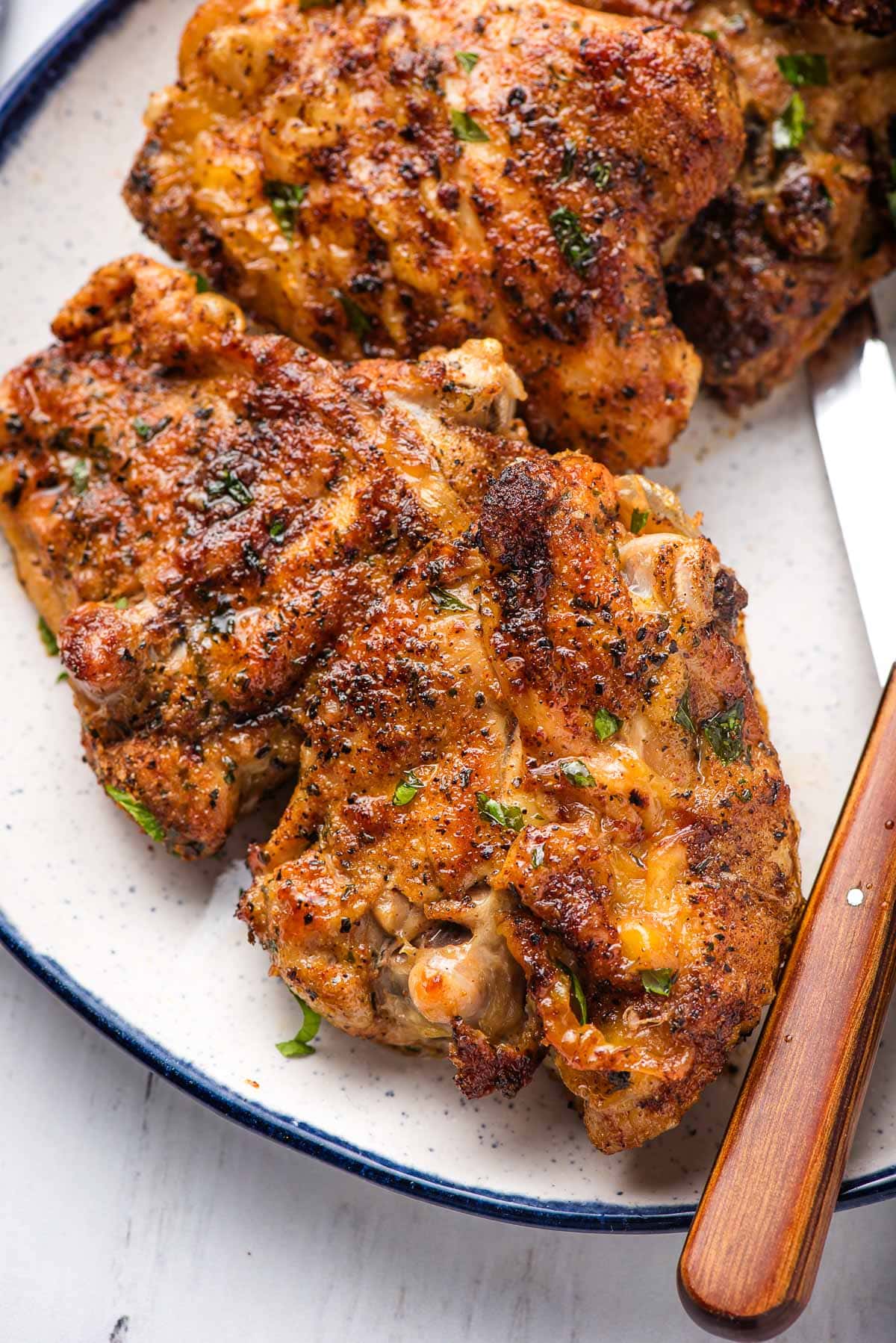 Bone in chicken thigh seasoned and air fried, on a blue rimmed white plate.