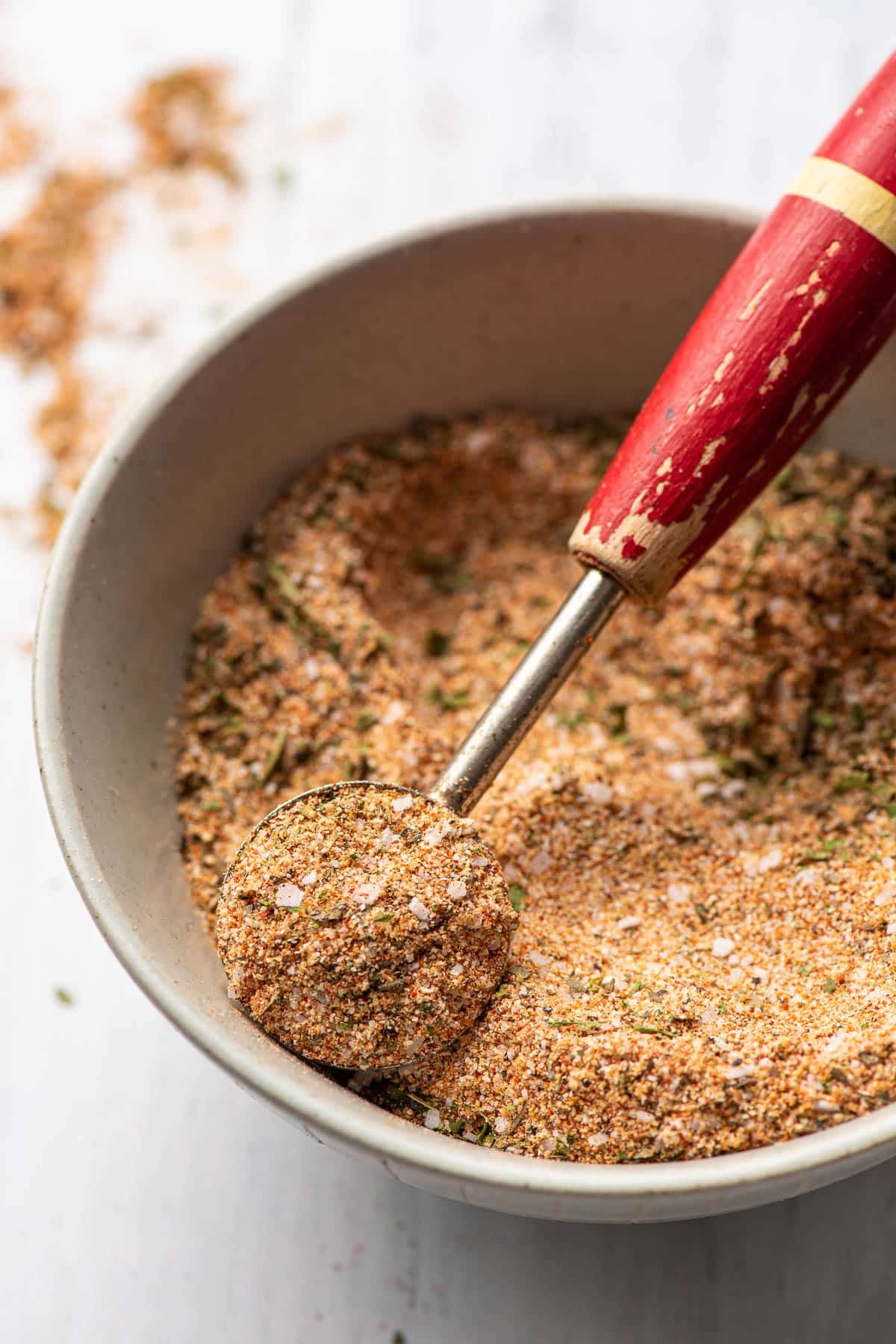 Vintage measuring spoon scooping up chicken spices from a bowl.