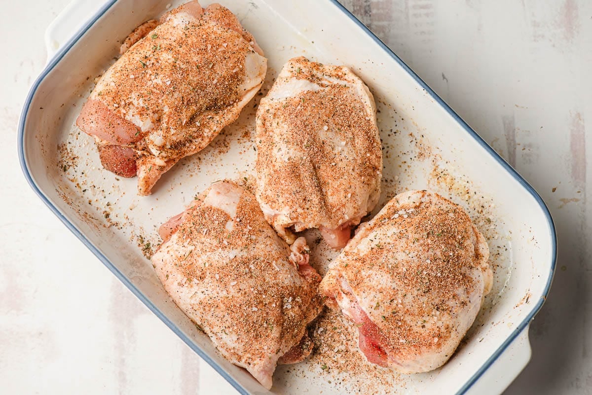 Seasoned skin on bone in chicken thighs in a casserole dish.