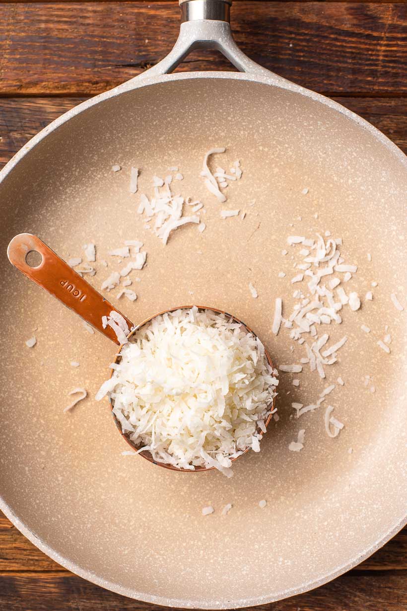 measuring cup of shredded coconut in a skillet