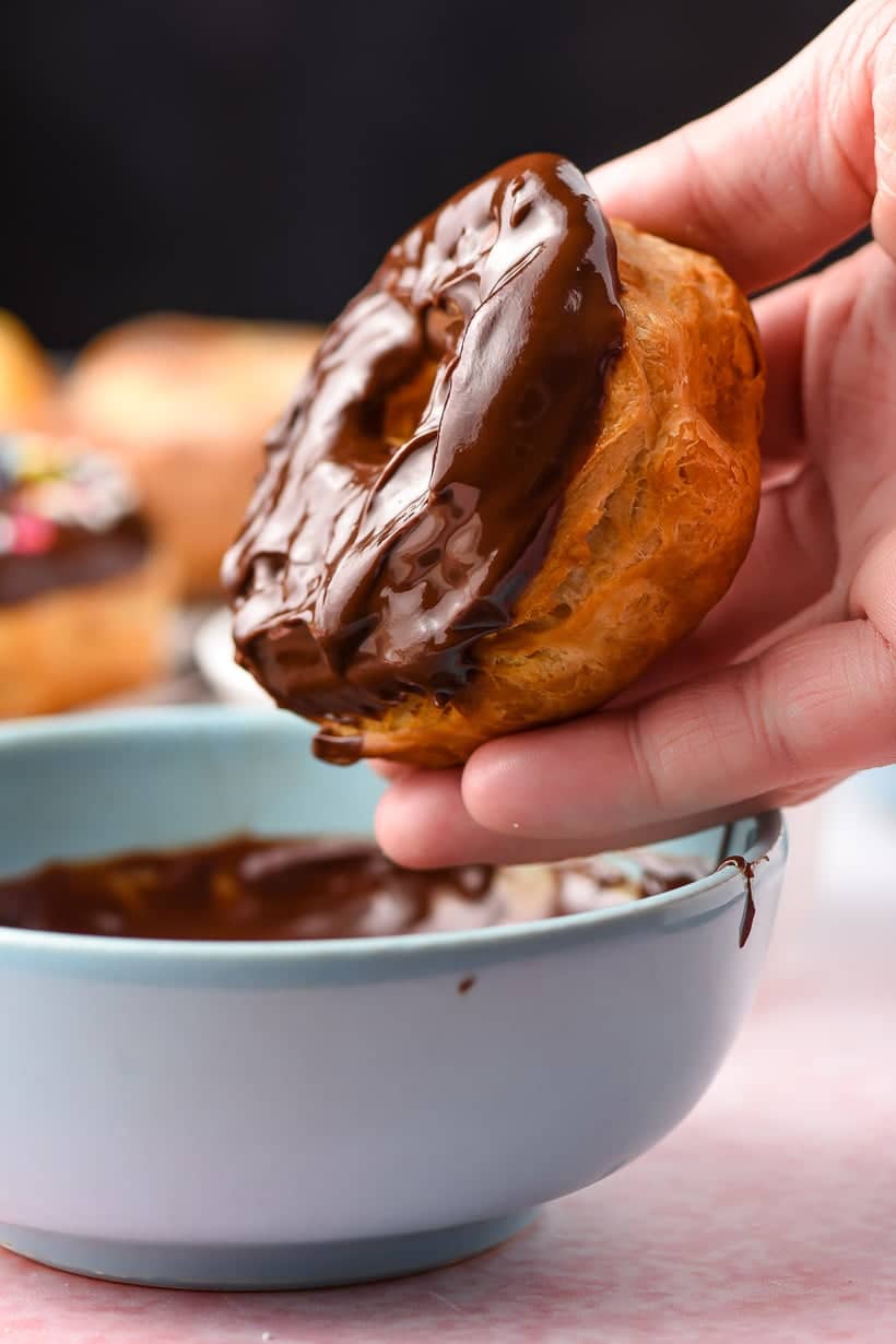 hand dipping air fryer donuts into chocolate glaze