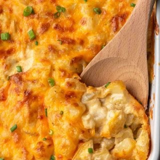 Wooden spoon scooping up cheesy potatoes from a casserole dish.