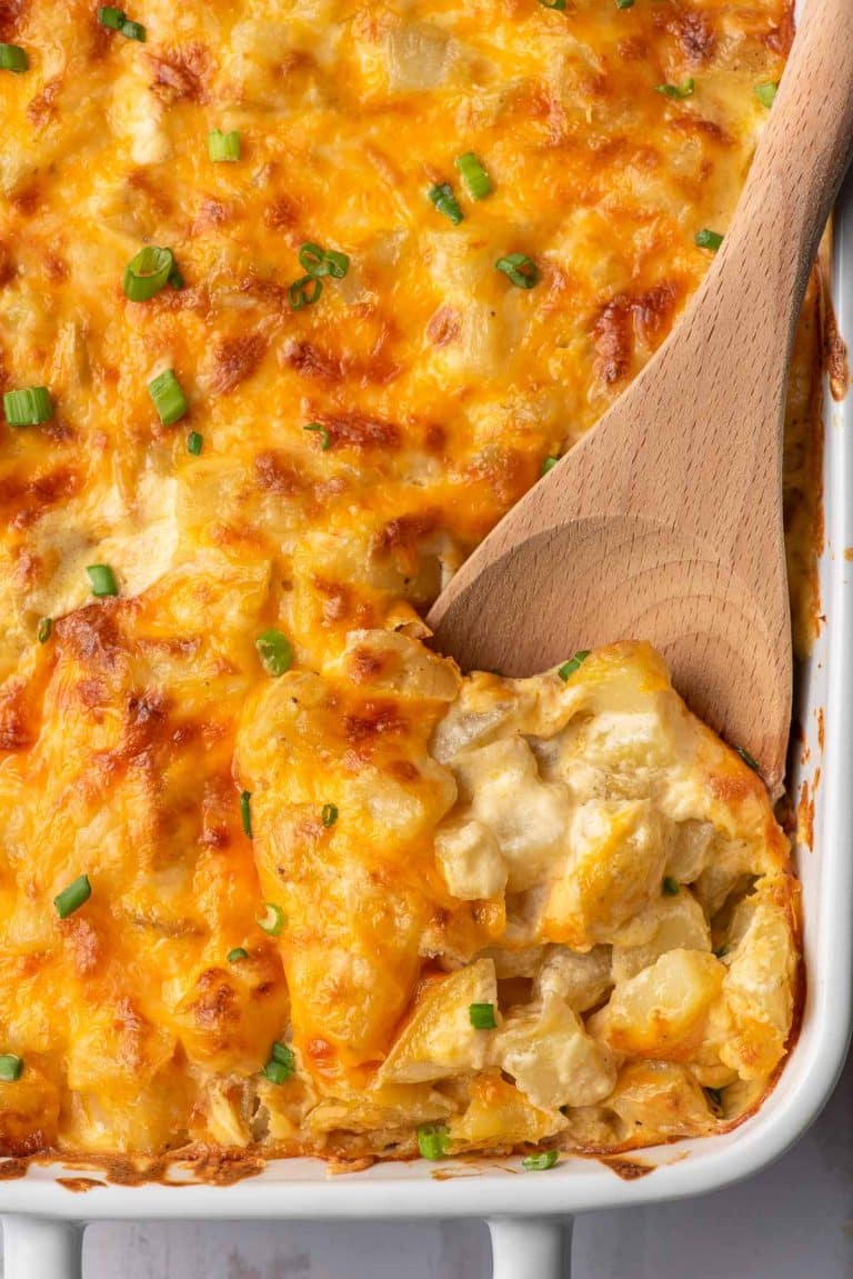Wooden spoon scooping up cheesy potatoes from a casserole dish.