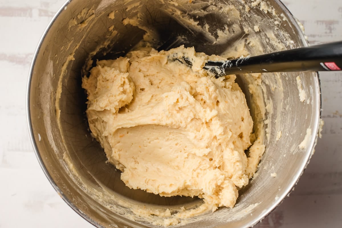 Orange cookie dough in a stainless steel bowl with a spatula.