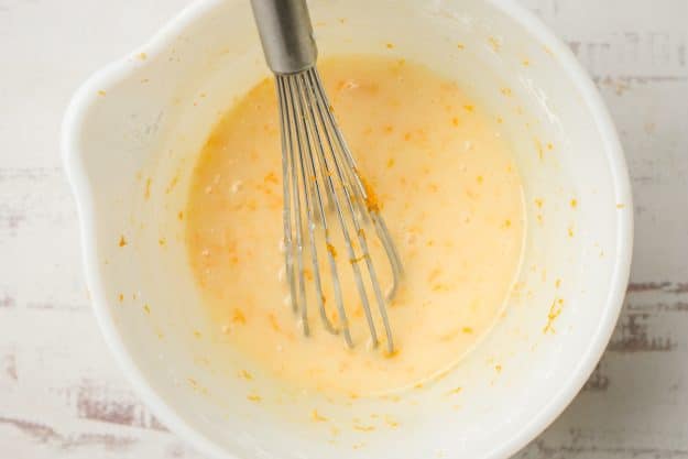 Orange glaze in a white bowl with a whisk.