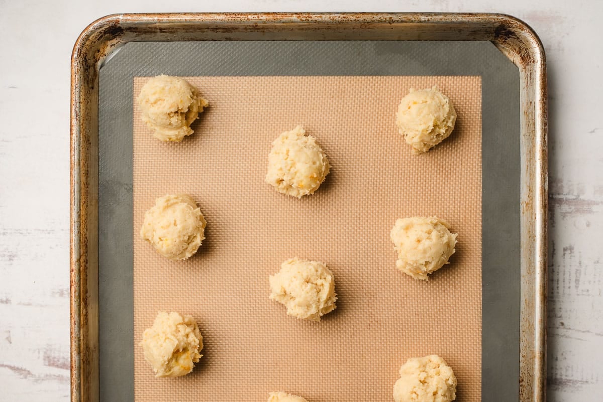 Orange cookie dough on a sheet pan lined with a silicone mat.