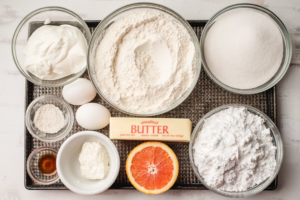 Ingredients in orange cookies, prepped in glass bowls, including eggs, dry ingredients, butter, and orange, cream cheese, and vanilla.