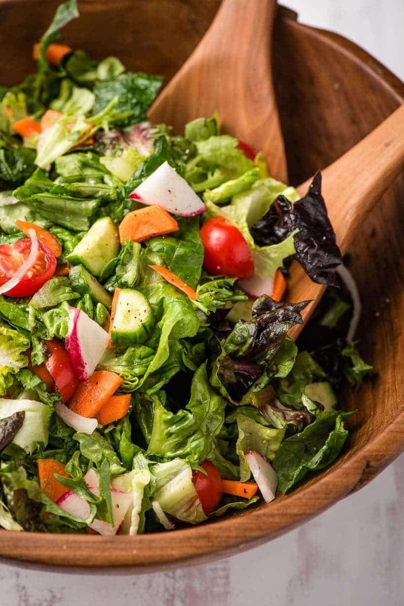 wooden bowl and salad servers scooping garden salad