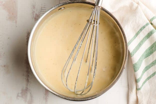 Homemade creamy white sauce with a whisk in a sauce pan.