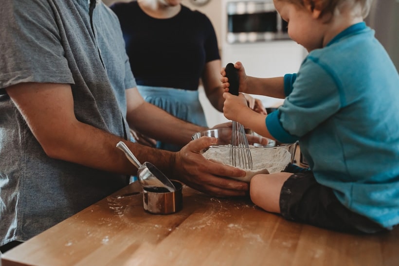 father, mother, and young child making a cake together