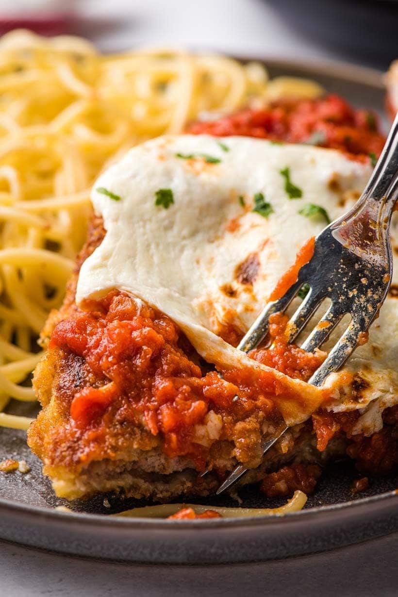 a fork taking a bite out of a piece of veal parmesan