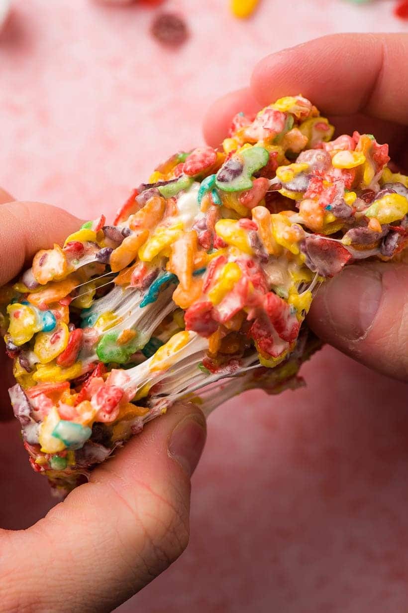 Hands pulling apart a Fruity Pebble Crispy Treat with strings of marshmallow