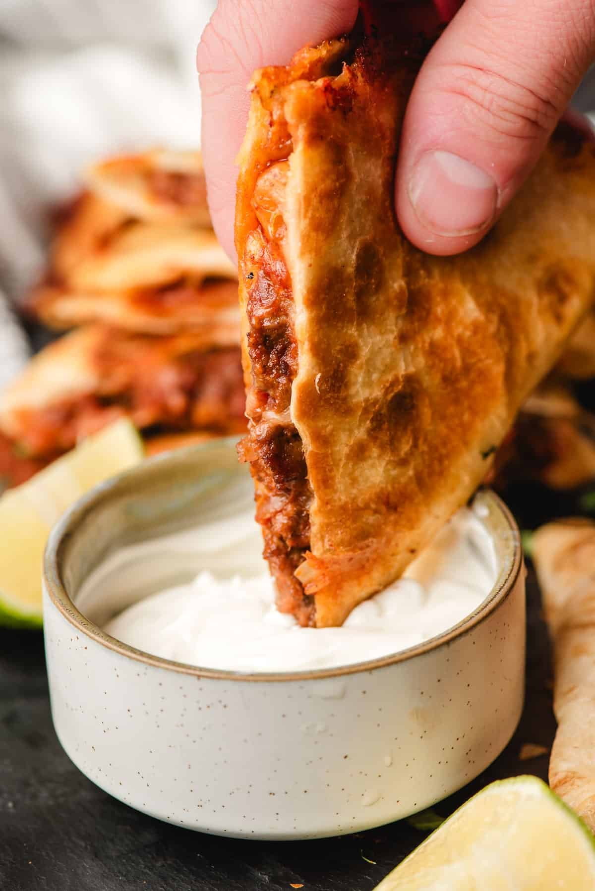 Ground beef quesadilla being dipped into a sour cream dip.