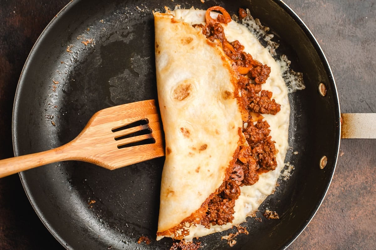 Wooden spatula flipping one side of a quesadilla over the other.