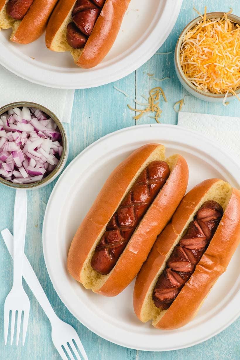 a table set with paper plates of air fryer hot dogs and toppings