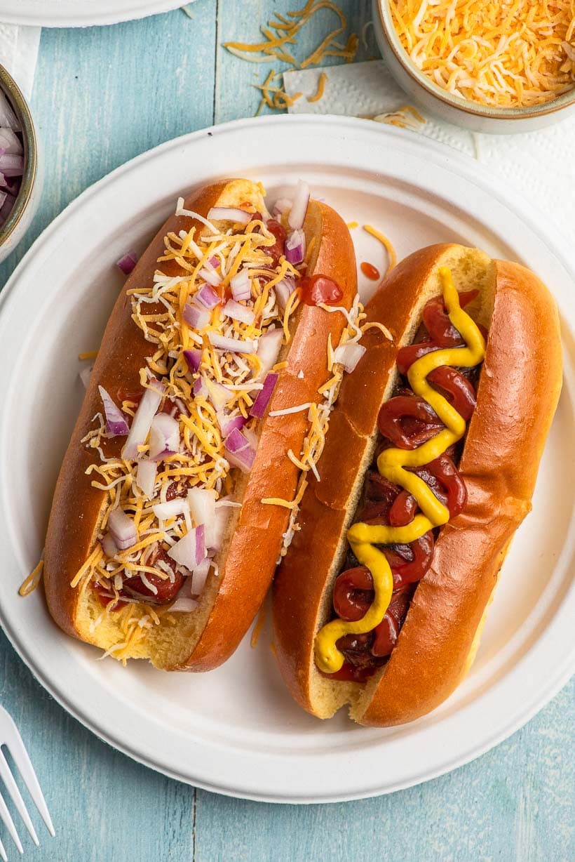 two fully topped air fryer hot dogs on a paper plate