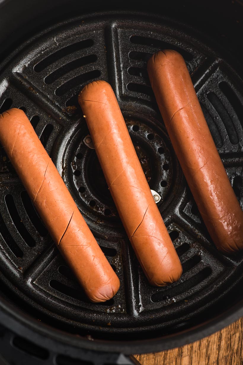 3 uncooked hot dogs in an air fryer